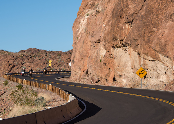 Motorcycles traveling on a curved road near a rock wall