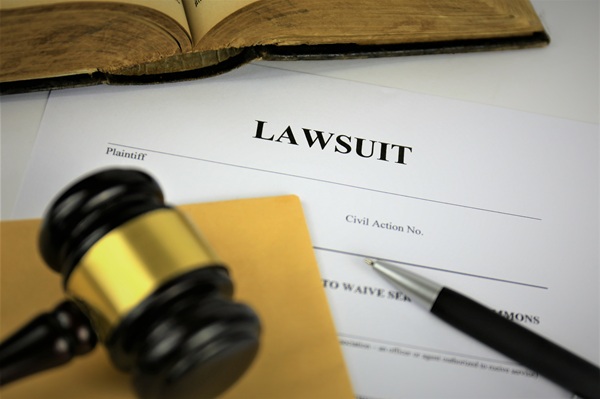 Court documents with the word “Lawsuit” at the top, next to a gavel, pen, and open book on a desk.