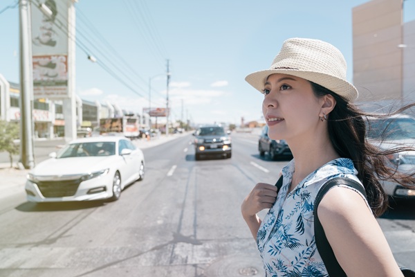 Woman with a backpack standing at a crosswalk in Las Vegas as cars pass by on a wide, busy road.