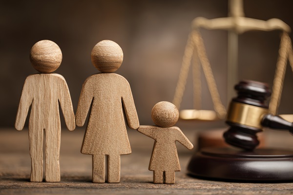 Wooden family figures stand before legal scales and gavel.