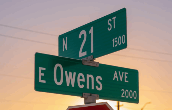 A street sign marking the intersection of N 21st St and E Owens Ave in Las Vegas against a rising sun.