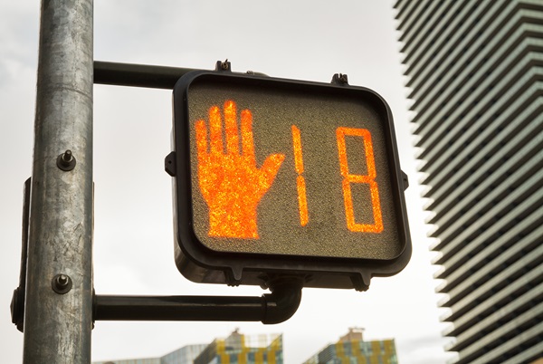 A pedestrian signal displays a glowing orange "hand" icon next to a countdown timer showing the number 18, set against a backdrop of tall city buildings in Las Vegas, Nevada.