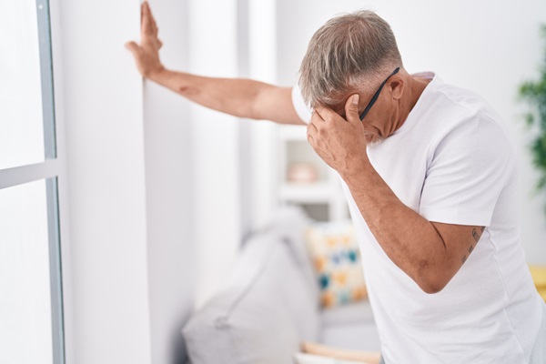 A man in a white t-shirt leaning one hand against a wall for support while holding his head with the other, capturing a moment of dizziness, loss of balance, or a severe headache following an accident in Las Vegas, NV, that resulted in a traumatic brain injury.